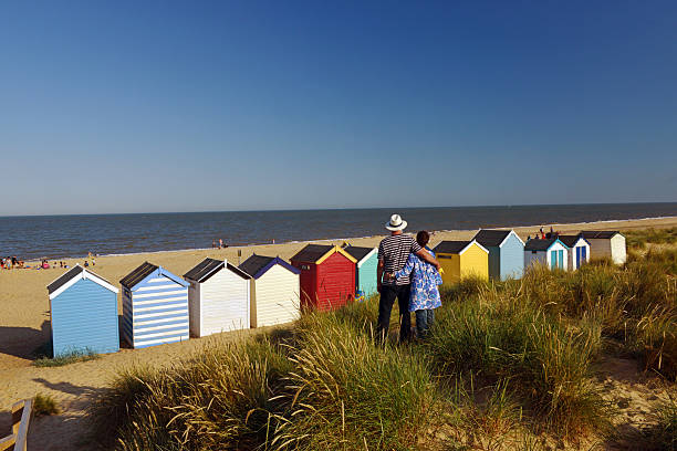 English Summer field Southwold,UK - August, 1st 2013: A couple standing on sand dune embrace overlooking the bathing huts lined along the beach southwold stock pictures, royalty-free photos & images
