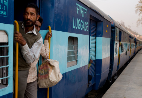 Haridwar, India - March 15, 2010 : man standing in the doorway of an indian train, hanging on to the hand rail, indian trains are generally full of people, well over their capacity