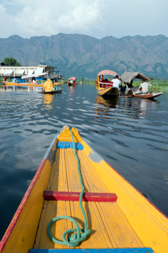 Srinagar, Lake Dal, Jammu and Kashmir, India - July 13th, 2011: Shikara boats used for carrying locals and tourists; white houseboat moored at the back. Everyday life in Lake Dal during tourist season.