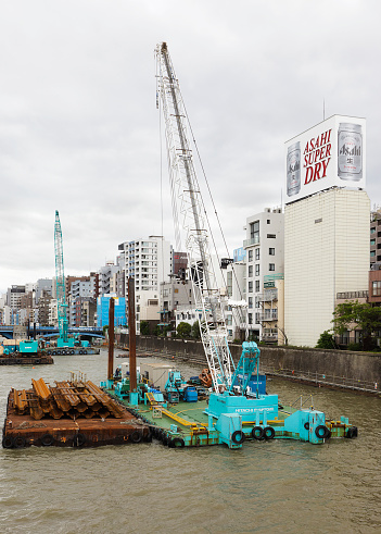 Tokyo, Japan - May 30, 2011: A construction crane mounted on a floating barge works near the seawall of the Sumida River adjacent to the Asakusa area of Tokyo. The Sumida River is a river which flows through Tokyo, Japan. It branches from the Arakawa River at Iwabuchi and flows into Tokyo Bay.