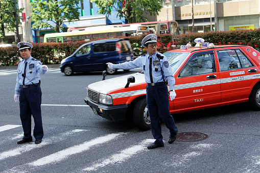 Tokyo, Japan - May 17, 2010: Japanese Police Officers are showing the right ways to the cars and pedestrians in Shinjuku, Tokyo. A taxi waiting for the pedestrian cross...