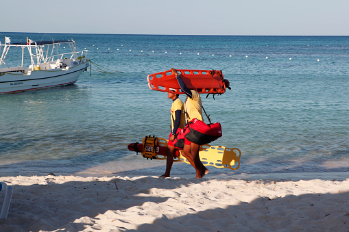 Riviera Maya, Mexico - April 23, 2012: Two Mexican lifeguards walks on a Riviera Maya beach at the end of the day with caribbean sea and a boat in the rear.