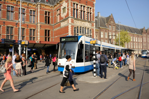 Amsterdam, the Netherlands - April 20, 2011: Two trams and a group of travellers in front of Amsterdam Central railway station. Most people in the image are waiting for or heading to a tram to get on. The local government discourages to drive a car in the Amsterdam city center, making public transport (tram, metro, bus) very important. In total there are 16 tramlines.