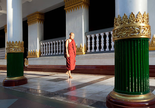 Yangon, Myanmar - February 16, 2011: A young monk walks alone inside the courtyard of the famous Shwedagon Pagoda. The famous Shwedagon Pagoda (also known as the Golden Pagoda) is the most sacred pagoda for Buddhists and is said to be 2500 years old. It enshrines relics from the past 4 Buddhas - 8 hairs from Gautama being the most sacred.