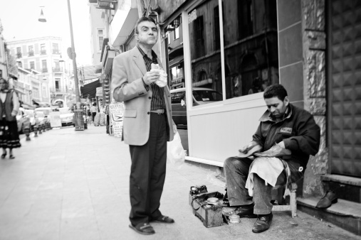 Istanbul, Turkey - November 5, 2009: A man has a bite to eat while waiting for a man to shine his shoes on the sidewalk in Istanbul.