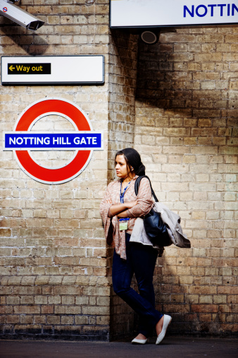 London, UK - May 3, 2011: Notting Hill Gate Underground Station, London. Woman wating for a train, standing on platform and leaning on wall arms crossed on chest.