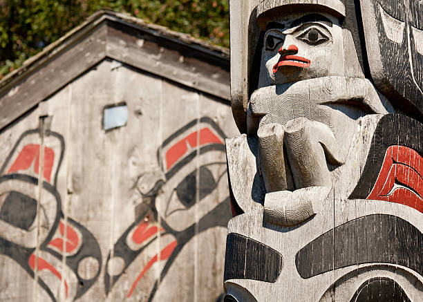 Haida Gwaii Totem Pole and Longhouse Masset, British Columbia, Canada - August 13, 2010: A detail of a Haida totem pole in front of a cedar longhouse building on Haida Gwaii, an island off the west coast of Canada. The rich texture is the result of years of exposure to the extreme weather on the island. haida gwaii totem poles stock pictures, royalty-free photos & images