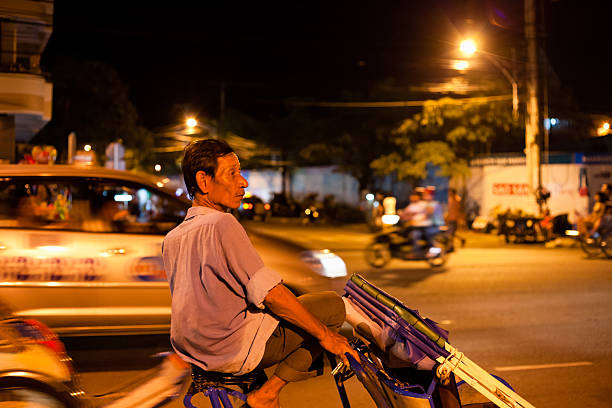 Man riding a Rickshaw in Nha Trang by night, Vietnam Nha Trang, Vietnam - July 16, 2011: Man riding a rickshaw in Nha Trang city by night, Vietnam. With taxis and scooters, rickshaws are common mode of public transportation in Vietnamese cities vietnamese old man portrait stock pictures, royalty-free photos & images