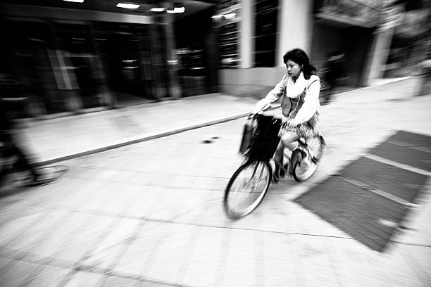 Tokyo, Japan - October, 25 2010: A japanese woman rides her bicycle down the sidewalk in the Shinjuku district of Tokyo. Motion blurred image with sharpest focus on woman's face.