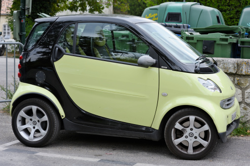 Dieulefit, France - August 14, 2011: Green Smart fortwo car in public car park with recycing bins in the background. Smart is a branch of German manufacturere Daimler AG and produces microcars, advertised as suitable for two people, for city life and for very low costs. They were developed from the need to find smaller cars which use less fuel and cause less ecological damage
