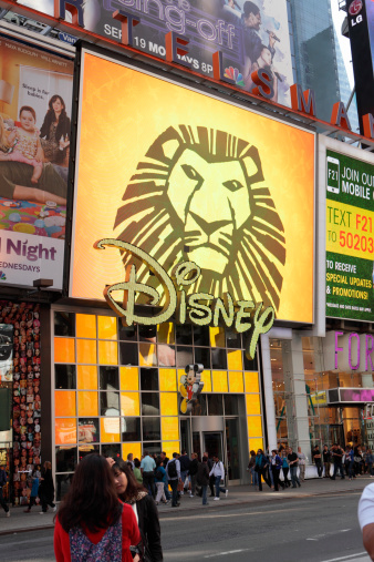 New York, NY, USA - September 17, 2011: View of the east side of Broadway between 46th and 45th Streets in Times Square, NYC. The video billboard above the Disney Store at 1540 Broadway advertises various shows and products, including the Lion King Broadway theater production displayed. Next door are other shops. Tourists and shoppers walk the sidewalks of Broadway in the morning.