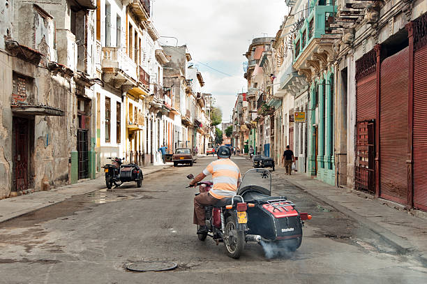 Havana, Cuba - January 1, 2011: Typical scene of one of streets in the center of La Havana in the morning -  old half-ruined colonial buildings, old cars and bikes are moving down the street, Cuban people are walking all around