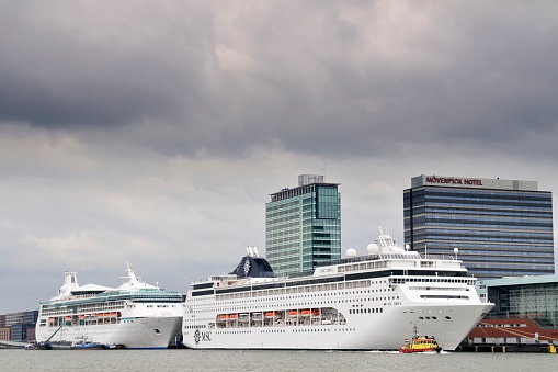 Amsterdam, The Netherlands - May 10, 2012: Two large cruise ships are docked at the terminal in Amsterdam, The Netherlands. MSC Lirica is moored in front of the Visions of the Seas. A small harbor boat is passing in the foreground.