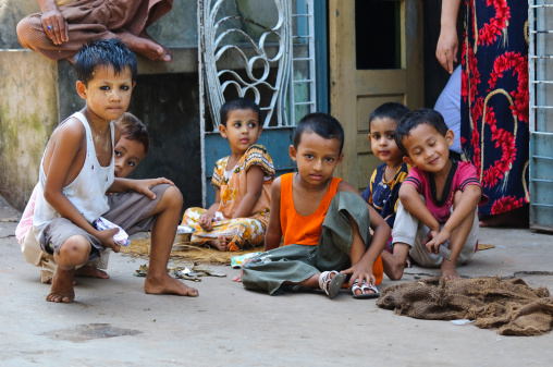 Mawlamyine, Myanmar - October 25, 2011: A group of Burmese boys and girls sit outside a home in the capital of Mon State. Two adults are in the background.