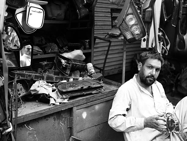 Karachi, Pakistan - June 17, 2010:  A Pakistani man siting beside body shop kiosks selling Rearview mirrors, speedo meters and other dashboard parts in Shershah Kabari Market (scrapyard) workshops in Karachi, Pakistan. Mostly Japenese and Korean Automobiles are imported as scrap after cutting in half and then disassembled here in pieses to sell as parts to save tax which is imposed on importing of complete vehicle. Located in old city area of metropolis Shershah's junkyard is home of few hundreds shops dealing in scrap items ranging from auto parts to industrial junk imported from developed world to recycle in foundries or to give another lease of life through this market.