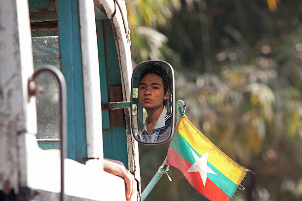 Life in Amarapura, Myanmar Amarapura, Myanmar - February 19, 2011:A young man driving a bus adorned with the new flag of Burma, looks out the side mirrors Amarapura, the former capital of Myanmar, means City of Immortality in Pali. It was founded after the court astrologers adviced the King to move the capital of the country to Amarapura after which the entire population of Inwa was asked to pack their belingings and migrate to the new land. Today the city is the center of weaving activities and is known to produce some of the finest festive clothing in Myanmar. Amarapura stock pictures, royalty-free photos & images
