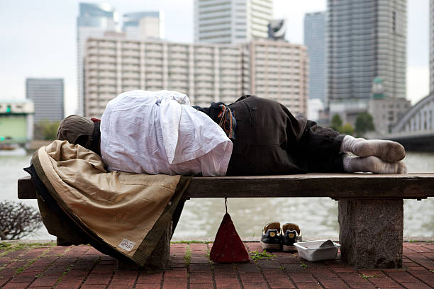 Tokyo, Japan - November 2nd, 2010 : A homeless Japanese man sleeps on a bench by the water.In the background modern high rises are visible.