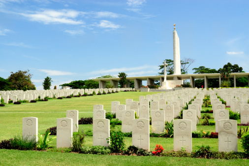 Kranji, Singapore - March 18, 2011: Kranji War Memorial and Cemetery. The image shows the the cemetery which contains the graves of over 4000 allied servicemen lost in WW2. The memorial (seen at the top of the hill),  is designed to represent land, sea and air forces, comprising columns (army), a wing (airforce) and the periscope of a submarine (navy). The cemetery is located close to Kranji Village in northern Singapore.