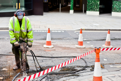 London, United Kingdom - September 10, 2011: A construction worker uses a jackhammer digging on a street. The worker is standing on the road, blasting concrete with the jackhammer.