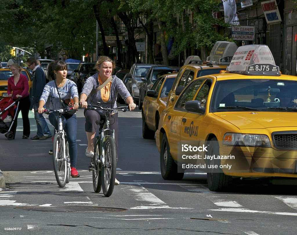 Biking in New York City, Greenwich Village, Manhattan New York City, USA - October 02, 2011: Two women on bicycles are seen entering the intersection of Christopher and Hudson Streets, following the designated bicycle lane markings along the street. They are riding alongside nearby taxis in West Greenwich Village, Manhattan. Active Lifestyle Stock Photo