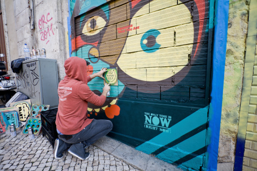 Lisbon, Portugal - November 10, 2011: Graffiti artist painting stencil art on the wall in the middle of the day. With many stencils around him, he is making this wall more colorful, or for some - ugly.