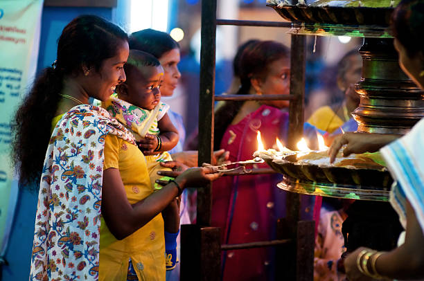 Young woman with child in the temple Kochi, Kerala, India - March 03, 2011: Young woman with a child lightening special candles in hindu temple in  Fort Cochin. Old hindu tradition at temple celebrations. Woman smiling and holding child in her hands. Night time. hindu temple in india stock pictures, royalty-free photos & images