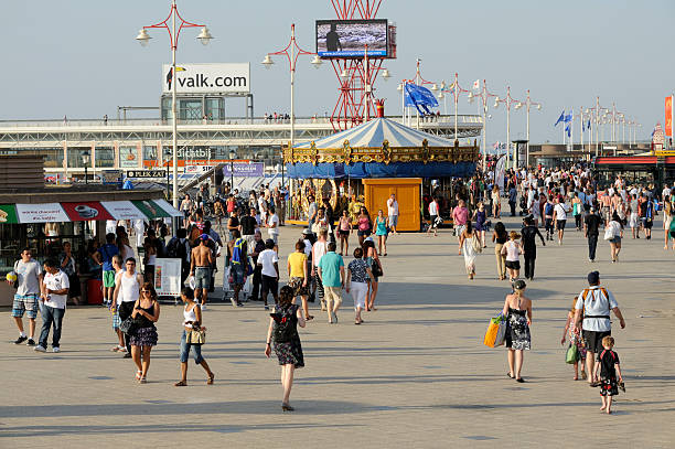 Scheveningen, The Hague, the Netherlands - June 27, 2011: People walking on the promenade at Scheveningen beach resort in the Netherlands. Scheveningen is a district and subdistrict of The Hague, located in the northwestern part of the city. The picture was shot two hours before sunset on a warm and sunny day. In the middle of the picture is a merry go round. At the background is the pier, leading over the beach, which is directly left to this scene. Scheveningen is the most popular beach in the Netherlands, yearly visited by 10 million people.