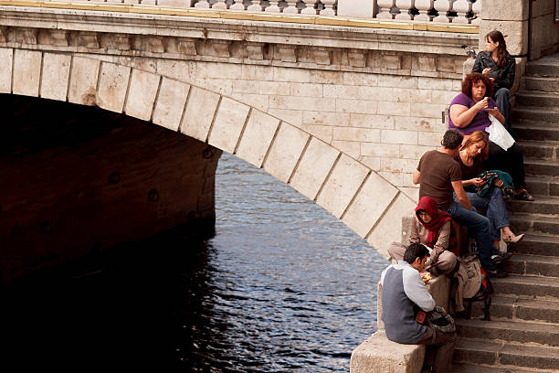 Paris, France - September 22, 2011: A group of people relax and have lunch outdoors in Pont Saint-Michel in Paris France. Eating take away food for lunch is becoming popular in big cities due to the stressful lifestyle in our time.