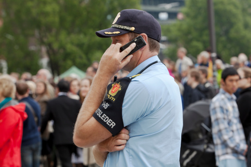 Oslo, Norway - June 16, 2012: Police man talking on mobile phone next to a group of people of mixed ethnicity.