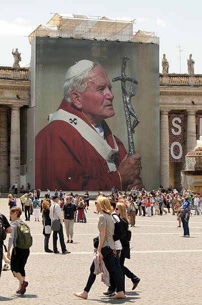 Pope John Paul II "Vatican City, Vatican City State - May 17, 2011: Tourists walk by a  large photograph of Pope John Paul II in St. Peter's Square." pope john paul ii stock pictures, royalty-free photos & images