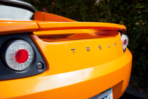 Palo Alto, California, USA - July 19, 2011: An exterior look at the rear end of an orange convertible Tesla Roadster electric sports car. The Roadster was designed in partnership with Lotus and debuted in 2008 and had a sticker price of around $100,000 dollars. Tesla plans to continue to sell the cars through 2012.