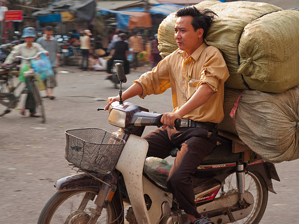 Hanoi, Vietnam - April 10, 2006: Man drives heavily loaded scooter through the street market in Hanoi, Vietnam. The bustle of the market can be seen in the background.