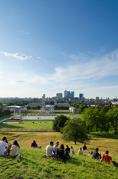 London, United Kingdom - July 24, 2011: Relaxing in Greenwich Park overlooking London. Young people relax in Greenwich Park on a summer afternoon and await the sunset. Greenwich Park is the oldest enclosed Royal Park and is situated on a hilltop, it has great views over London including the Naval College, Canary Wharf, the Millennium Dome and the skyscrapers of the city of London.