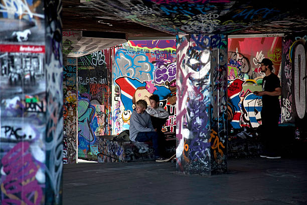 London, UK - May 2, 2011: The Skatepark, Southbank, London.  Two youths and a young adult watch skateboarders and BMX riders.  The graffiti walls are constantly added to and change from week to week. The skatepark is under the Southbank Centre on London's embankment and popular with skateboarders and BMX riders.