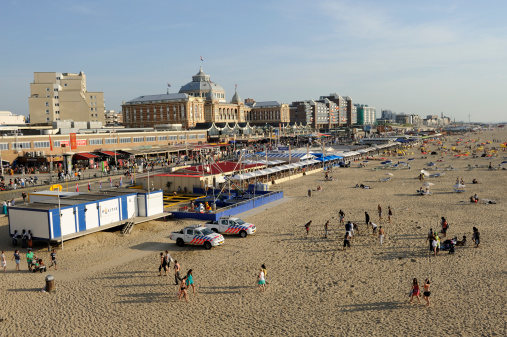 Scheveningen, The Hague, the Netherlands - June 27, 2011: Scheveningen beach resort. Scheveningen is a district and subdistrict of The Hague, located in the northwestern part of the city. The picture was shot two hours before sunset on a warm and sunny day. From right to left are a long sandy beach, restaurants, and a promenade with shops, restaurants and hotels. The second, large building at the background is the Steigenberger Kurhaus Hotel.At the left of the picture is a mobile police station and two parked police cars in front of it.Scheveningen is the most popular beach in the Netherlands, yearly visited by 10 million people.