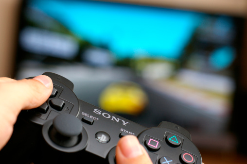 Wejherowo, Poland - July 4, 2011: Man\'s hand holding Sony Dualshock wireless controller while playing Gran Turismo 5 on Playstation 3.