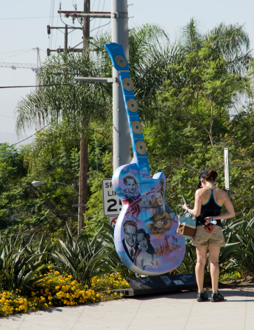 West Hollywood, California, USA - August 27, 2010: A woman pedestrian stops to take a look at one of the many uniquely decorated ten foot tall Gibson guitar replicas on display on Sunset Boulevard in West Hollywood.
