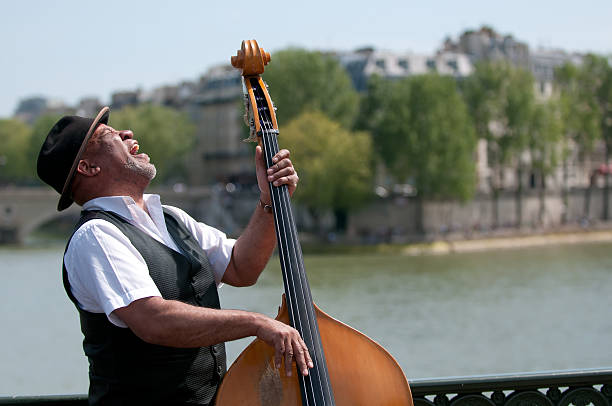 Black man playing an acoustic bass Paris, France - May 3, 2008: Street artist playing Double Bass in paris. In the background you can see the Seine. The Seine is a major river and commercial waterway in France. double bass stock pictures, royalty-free photos & images
