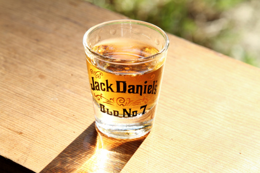 West Palm Beach, USA - September 17, 2011: This image shows a shot glass with the Jack Daniels brand name and design filled with Jack Daniel's Old No 7 Whiskey. The shot glass is setting on an outdoor wood bench with the late afternoon sun shining through and illuminating the whiskey.