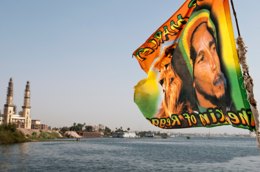 Aswan, Egypt - April 4, 2010: A Bob Marley flag flies from the back of a felucca on the Nile River near Aswan. The text says: The King of Reggae. On the bank of the river is a mosque under construction.