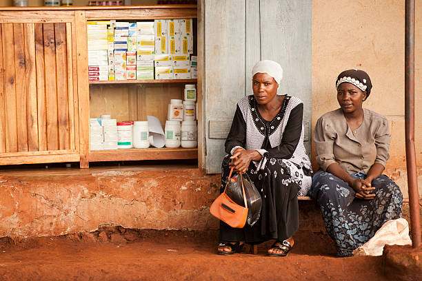 African Women are sitting Hoima, Uganda - November 18, 2011: Two African Women are sitting near the mini drugstore and they are waiting. uganda stock pictures, royalty-free photos & images