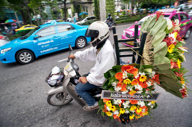 Bangkok, Thailand - August 29, 2011: A motorcycle delivery rider leave a Sukhumvit Road flourist to deliver large arrangements of colourful flowers.