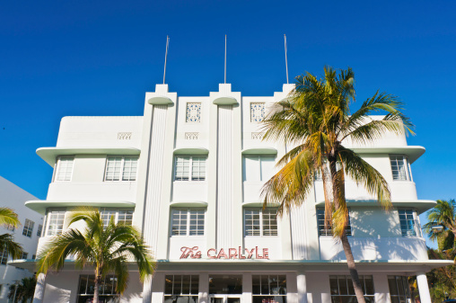 Miami, Florida - December 13th, 2008: Iconic Art Deco hotel The Carlyle\\'s pastel stucco gleaming in the Florida sun under deep blue skies beside the palm trees of Ocean Drive in Miami Beach.