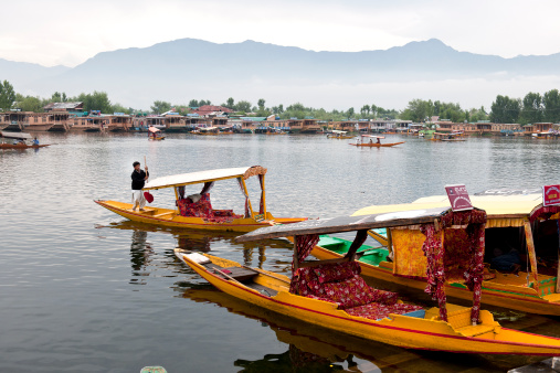 Srinagar, Lake Dal, Jammu and Kashmir, India - July 14th, 2011: Shikara boats, used for carrying locals and mostly tourists, in  front; houseboats(hotels) moored at the back. Everyday life in Lake Dal during tourist season.