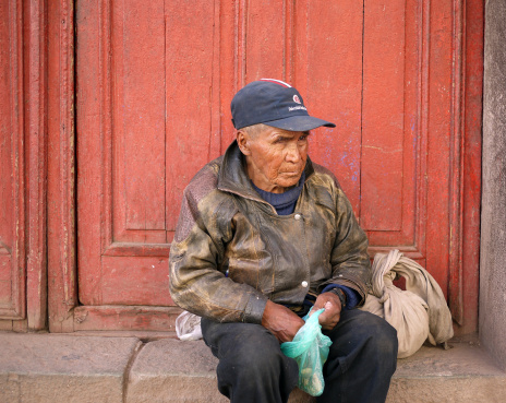 Cusco, Peru - December 14,2009: Visually impaired, peruvian beggar sitting in front of a door at street of Cusco. He is holding a plastic bag.