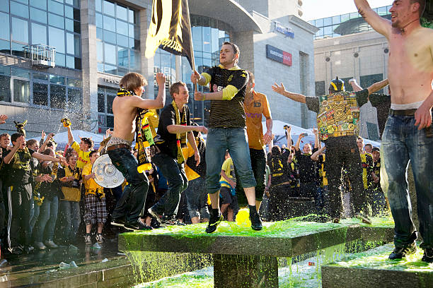 Dortmund, Germany - May 14, 2011: Soccer fans are celebrating their club Borussia Dortmund  (BVB 09) winning the German league title in the season 2010/11, over Eintracht Farnkfurt. Everybody is wearing black and yellow, the colors of the club. They had climbed into a fountain on &ldquo;Alter Markt&rdquo; in Dortmund downtown, the water was colored yellow to celebrate this event. They are waving flags and are splashing the water.