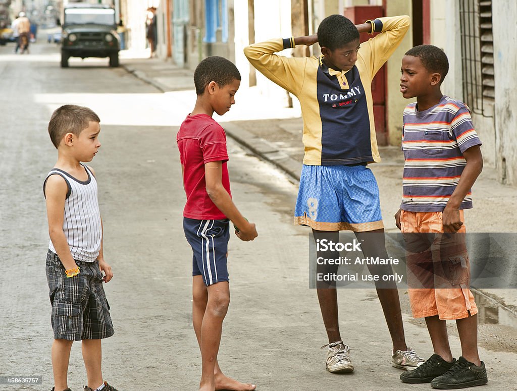 Havana street, Cuba Havana, Cuba - January 1, 2011: Four Cuban children standing at one of narrow streets in the center of La Havana. Colonial architecture, old car parked at the street, Cuban people walking all around. Boredom Stock Photo