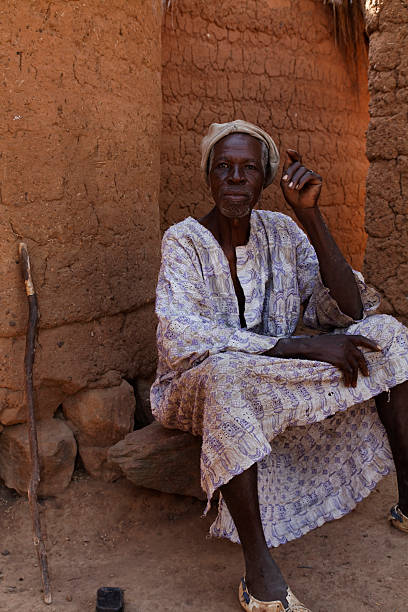 african village headman resting in the shade of his hut - boubou stockfoto's en -beelden