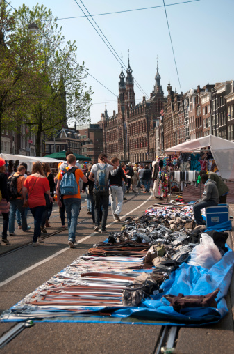 Amsterdam, Netherlands - April 30, 2011: The streets of Amsterdam transformed into a giant flea market (Vrijmarkt) on Queen's Day (Koninginnedag). Major roads are closed off to become pedestrian zones. Pedestrians walk by a temporary stall with belts, handbags, and other products.
