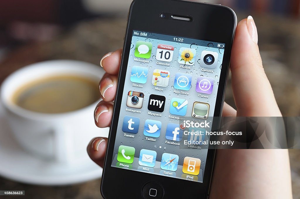 Woman holding iPhone in a coffee shop İstanbul, Turkey - November 10, 2011: Woman hand holding an Apple iPhone 4 in a coffee shop. iPhone 4 displaying the home screen with social media apps. The iPhone 4 is a touchscreen slate smartphone and the fourth generation iPhone, developed by Apple Inc. Coffee Shop Stock Photo